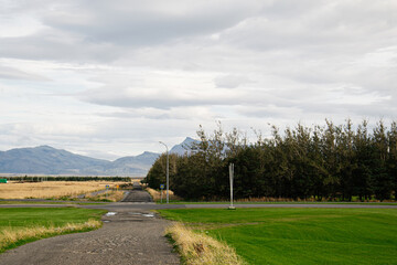 Obraz premium Rural road with mountain landscape and trees under a cloudy Icelandic sky