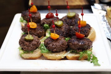 bandeja de pinchos de carne en formato mini hamburguesas con ingredientes de tomate Cherry y pepinillo