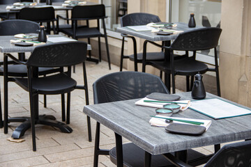 Outdoor dining area featuring modern black chairs and tables set with menus and utensils, creating a stylish and inviting atmosphere for patrons to enjoy meals