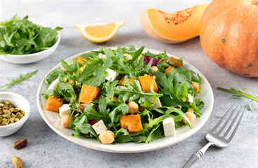 Healthy green salad with arugula, pumpkin, feta cheese, chickpeas, pistachios on a gray background.