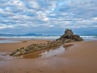Twilight seascape with dramatic, cloudy skies - A tranquil scene of a rocky beach at twilight with soft light reflecting on the sand and calm ocean under a moody sky.