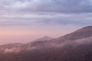 Hambacher Schloss im herbstlichen Sonnenaufgang mit Nebel und Wolken über dem Pfälzerwald