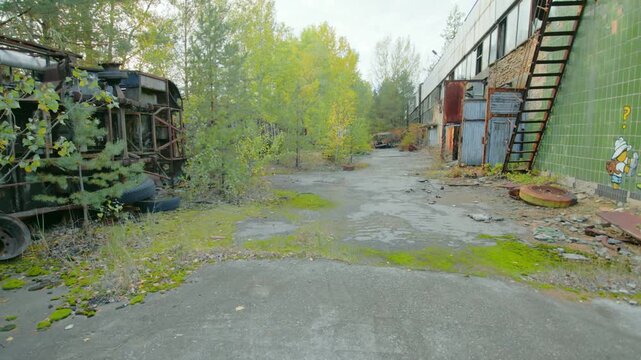 Footage capturing the eerie and desolate scene of an abandoned motor transport establishment within the Chernobyl Exclusion Zone, near Pripyat, Ukraine. Overgrown vehicles and buildings stand as a tes
