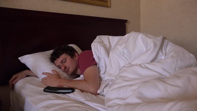 Man sleeping with TV remote in hotel bed 4k