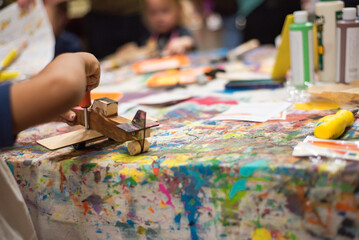 Rear view close-up of Asian boy using a screwdriver to attach wood to a wooden airplane, surrounded...