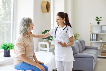 Friendly female doctor comforting elderly patient sitting on couch in hospital. Warm and caring physician or cardiologist providing support to senior woman, cheering her up during medical checkup.