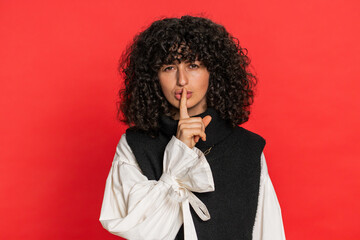 Shh be quiet please. Caucasian woman presses index finger to lips makes silence gesture sign do not tells secret, stop talk gossip, confidential privacy. Pretty young girl isolated on red background