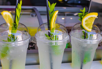 Lemonade in plastic cups with a plastic straw, lemon slice and small green branches