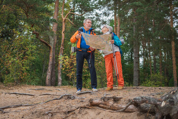 Hiking tourism. Senior couple man woman looking track in paper map enjoying hiking in forest. Happy old people backpackers hikers enjoy walking hike trekking tourism active vacation beauty of nature
