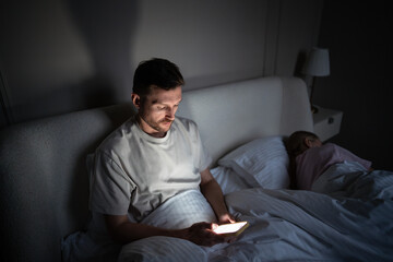 Cheating husband scrolls phone, chats on social networks, messaging in bed at night. Wife sleeps...