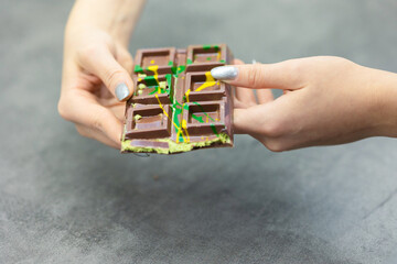 Female hands breaking off piece of Dubai chocolate on gray background. Green kadayif and pistachio spread with pistachio in trend dessert. Close-up, selective focus. High quality photo