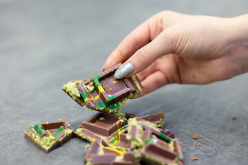 Woman's hand holds piece of Dubai chocolate on gray background. Green kadayif and pistachio spread with pistachio in trend dessert. Close-up, selective focus. High quality photo