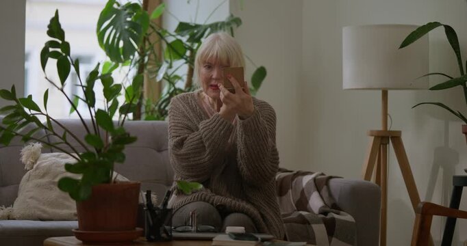 Elderly woman applying powder on face during makeup in cozy apartment. The Signor woman maintains her beauty and loves her age