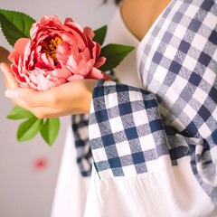 Woman holding a pink flower, wearing a white and navy gingham top