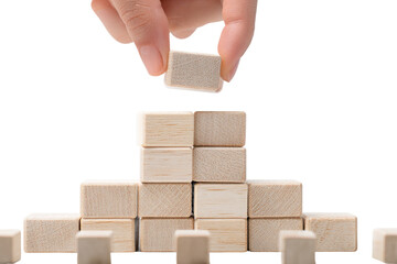 A hand carefully places a light beige wooden block atop a growing stack of similar blocks.  The blocks form a small pyramid-like structure