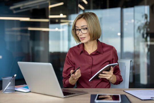Businesswoman working on laptop and taking notes during video conference in office