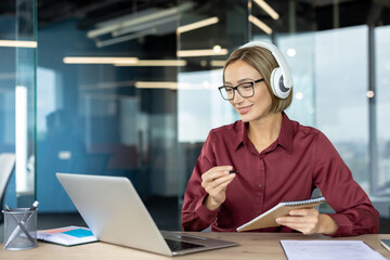 Businesswoman working from office using laptop and headphones
