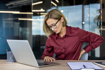 Businesswoman suffering from back pain while working on laptop in office