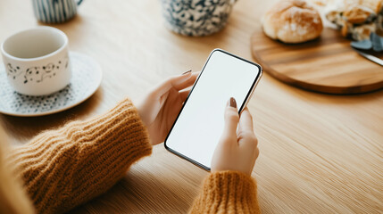 Woman hands in yellow sweater using phone or smartphone with white screen mockup with empty space for text sitting at table in cozy cafe.