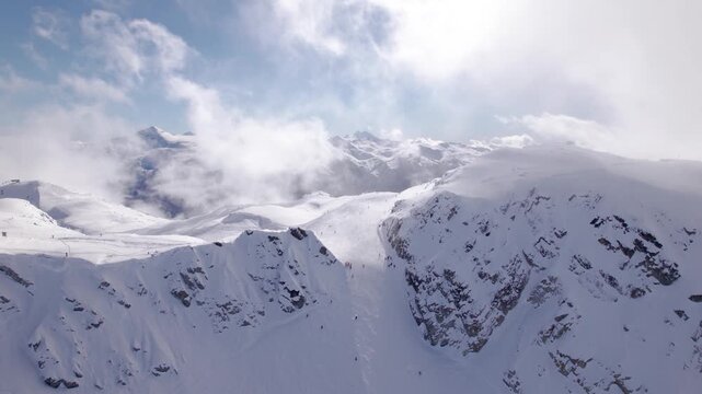 Aerial view of Whistler Mountain peak, downhill skiers, sunny snow covered peak, ski resort. 4K 24FPS