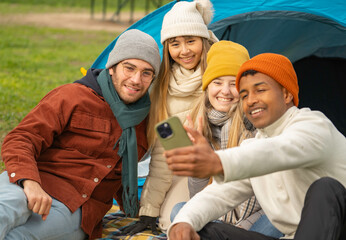 Multiethnic group of four happy friends are taking a selfie in front of a tent while camping