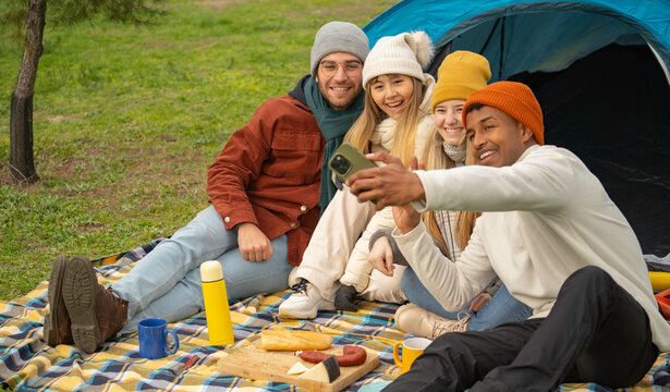Multiethnic group of happy friends taking a selfie during a camping trip, enjoying a picnic in front of their tent