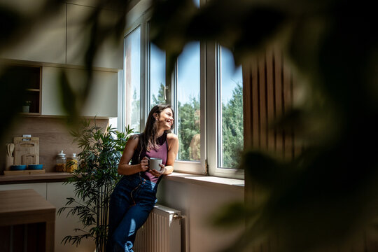 Young woman enjoying a cup of coffee by the window in a modern kitchen