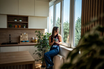 Young woman enjoying breakfast while sitting by window in modern kitchen