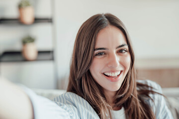 Naklejka premium Young happy and cheerful woman taking a selfie smiling looking at the camera, enjoying free time at home working and studying indoor in office