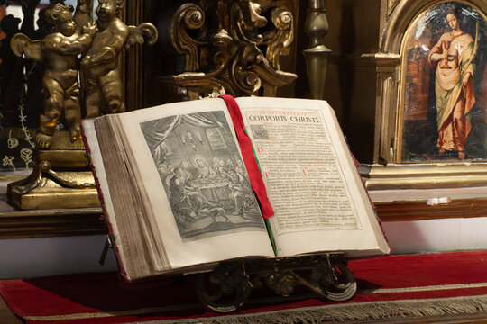 A book is open to a page with a red ribbon. The ribbon is tied to the book, and the book is on a stand. The book is old and has a gold frame. City of Puebla, Mexico, crafts - Powered by Adobe