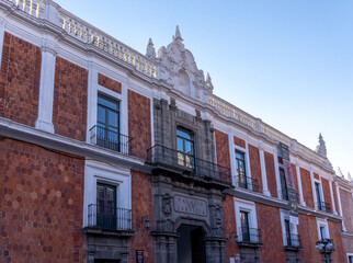 A large building with a red brick facade and white trim. The building has a balcony and a large window. City of Puebla, Mexico, crafts