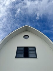 Minimalist house facade with window and roof against bright blue cloudy sky