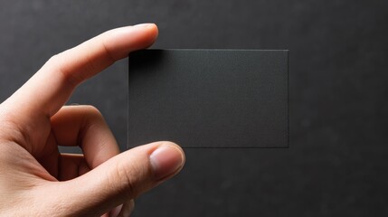 Blank business card being held by a hand against a dark background in a minimalistic setting