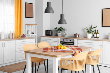 Interior of beautiful kitchen with white counters, dining table, fruits, chairs and lamps