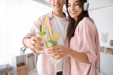 Happy young couple in headphones with glasses of mojito at home