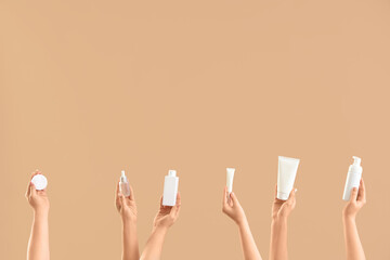 Many female hands with bottles of cosmetic products on beige background
