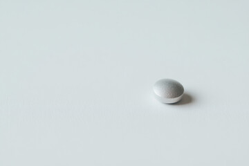 Minimalist close up of a single gray tablet resting on a clean white surface, soft shadow, simple composition, medical theme, calm clinical mood.