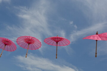 A line of vibrant pink umbrellas suspended against a bright blue sky with wispy clouds