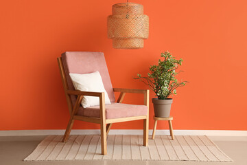 Pink armchair and houseplant near orange wall in interior of room