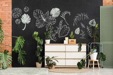 Stylish interior of living room with white chest of drawers, tropical plants and chalk drawing on...