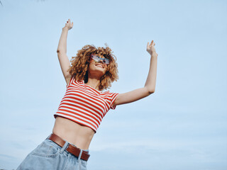 A joyful person with curly hair wearing a striped red and white top and denim jeans stands against...