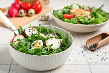 Bowl with tasty arugula salad on white tile background, closeup