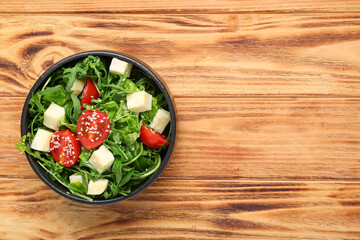 Bowl with healthy arugula salad on wooden background, closeup