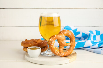Board with pretzels and glass of cold beer on white wooden background, closeup