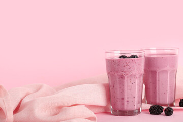 Glasses of fresh blackberry smoothie and berries on pink background