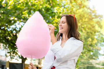 Beautiful young happy woman with cotton candy in park, outdoors