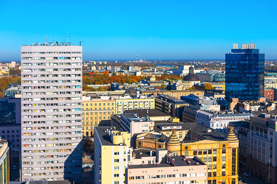 Aerial view of Warsaw shows a dense urban landscape with a mix of old and modern buildings, including a tall apartment block and a glass skyscraper. Panoramic view of a city skyline in autumn