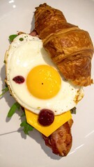 Gourmet Croissant Sandwich with Fried Egg, Cheese, and Bacon on a White Plate