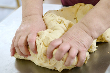 Hands kneading cracker dough on a stainless steel surface in a cozy kitchen environment during daytime preparation