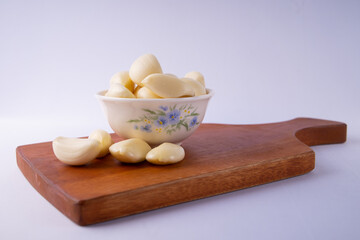 Fresh peeled garlic cloves in a white bowl on wooden cutting board, natural spice for cooking, seasoning, herbal medicine, and healthy organic food ingredient